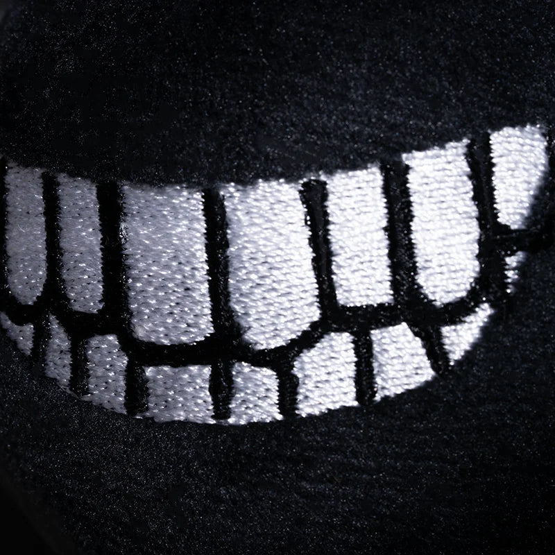 close up view of a black, plush eyeless figure's white, toothy smile