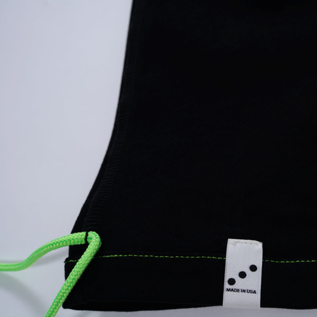 The corner of a black t-shirt with two green string and a white MADE IN USA label on a light gray background