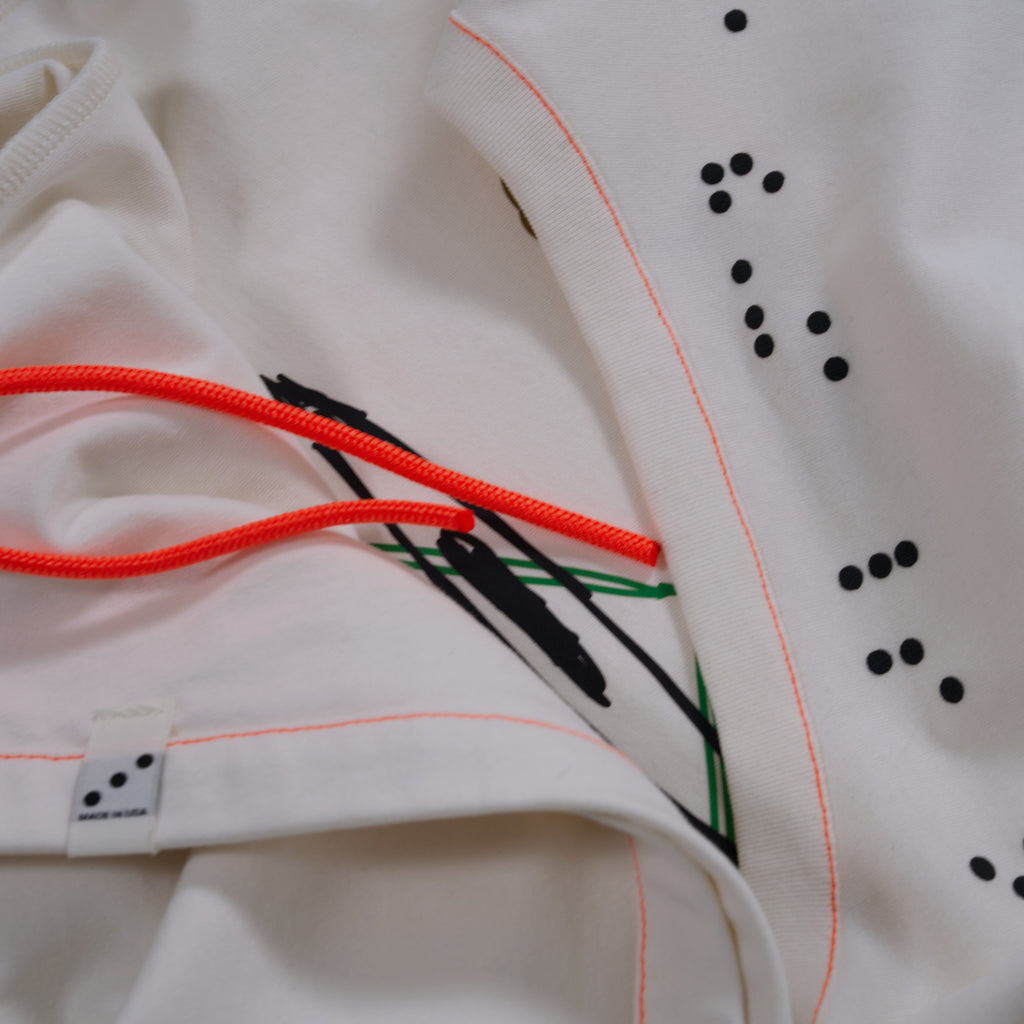 Close-up of a white garment with black and green embroidery and orange cord, on a light background.