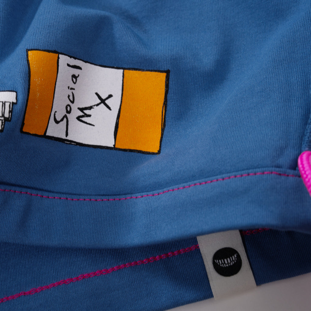 Close-up of blue fabric from a t-shirt with a graphic of a pill bottle and brand tag with a smiling eyeless graphic