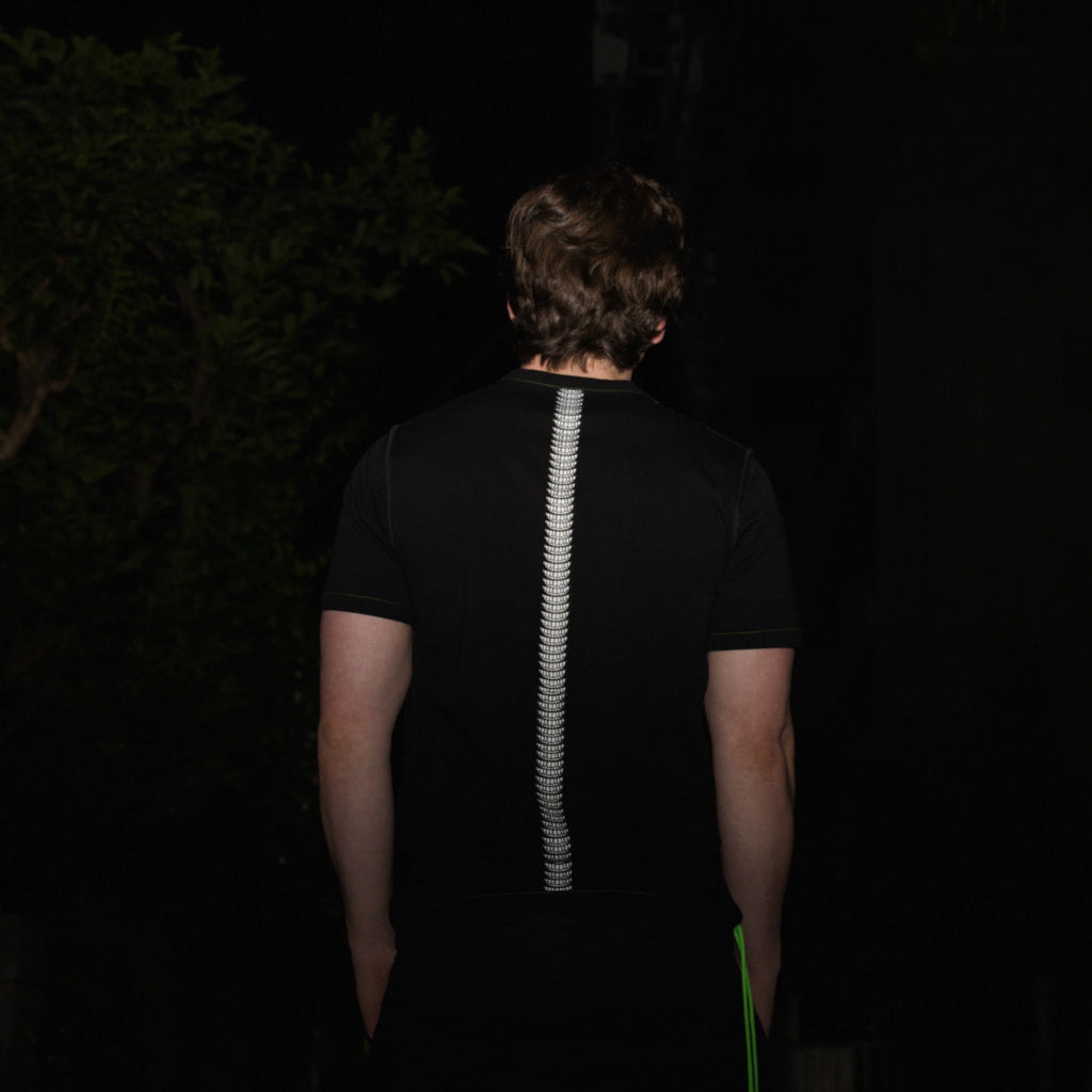 Person wearing a black normal;c movement t-shirt with a white smile design on the spine of the shirt, standing in a dark outdoor setting.
