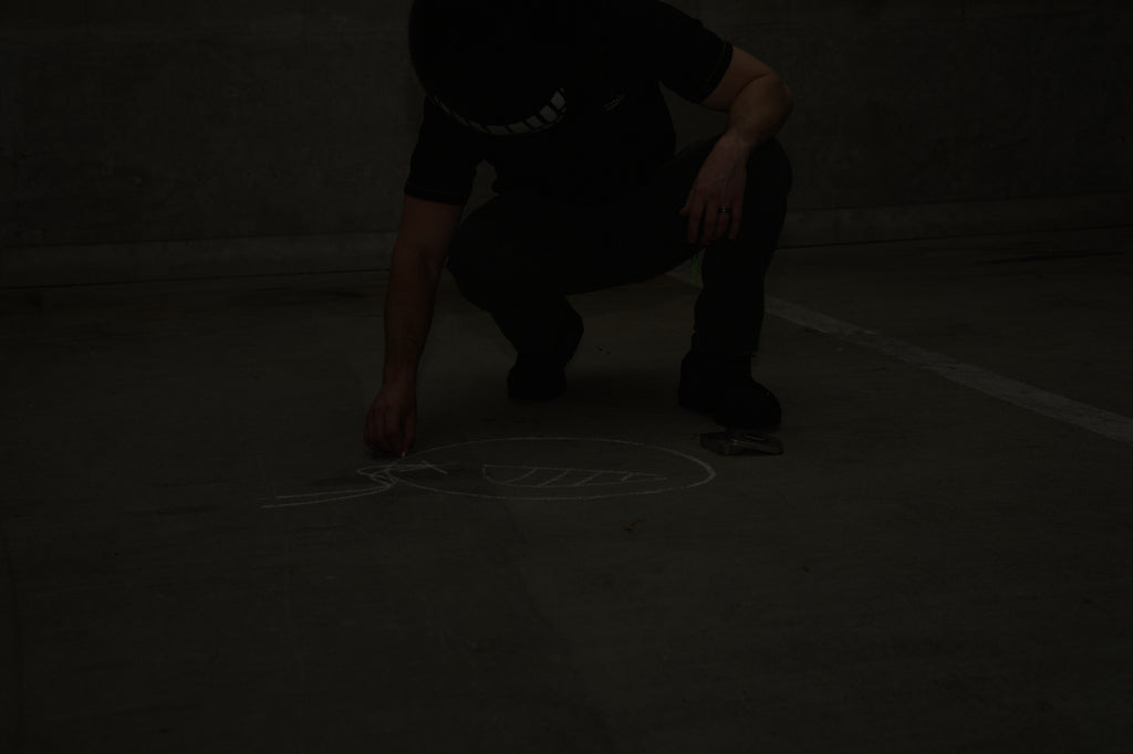 Person crouching on a dark floor  of a garage with a light drawing on the ground